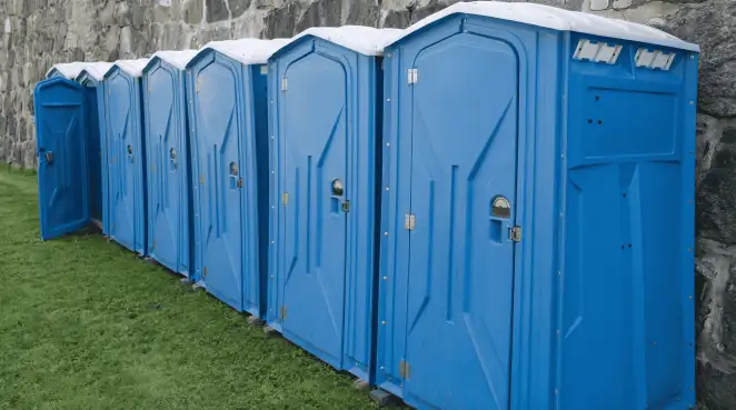 Row of blue portable toilets lined up on grass against a stone wall for event sanitation in Lakeland, FL
